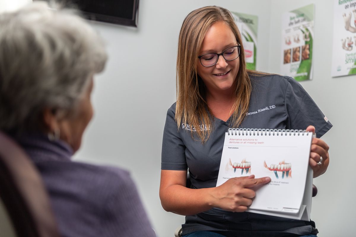 The image of the owner of the Rizzoli Denture and Implant Clinic holding up an illustration of a denture to a denture patient