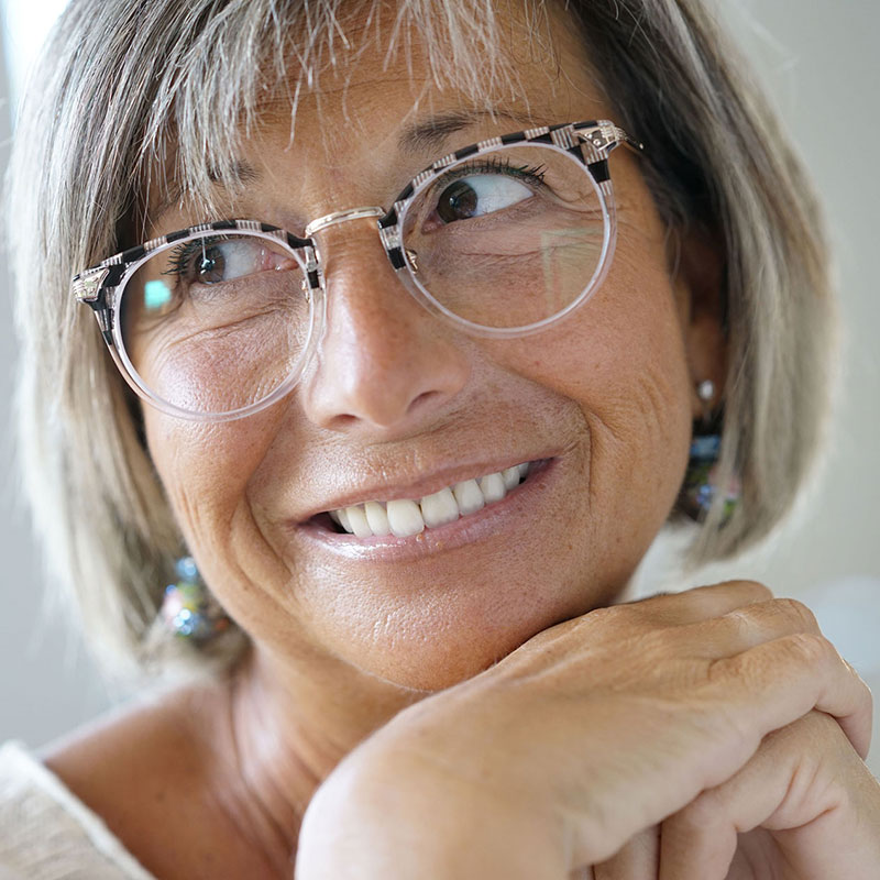 A close-up image of a mature lady leaning her chin on her clasep hands and wearing a pair of funky eye glasses