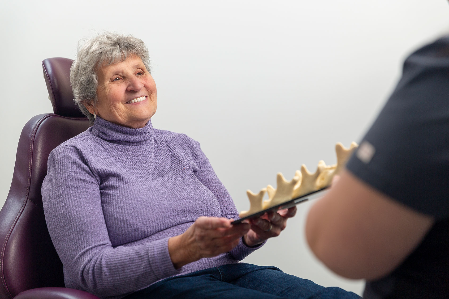 A happy patient at Rizzoli Denture & Implant Clinic holding a tray of jaw samples