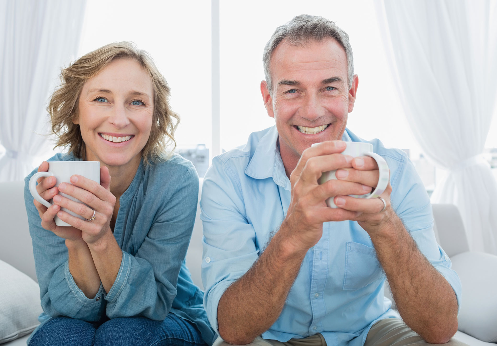A smiling couple wearing lower suction dentures having coffee